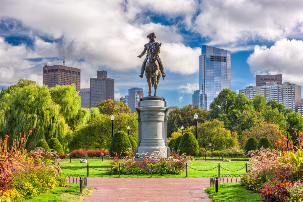 Statue of George Washington on horseback at the entrance of Boston Public Garden with Boston's Financial District in the background.